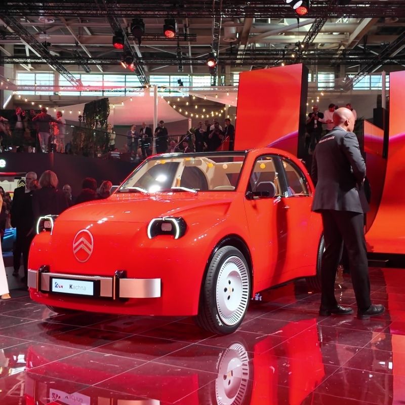 Orange Citroën 2CV Concept with white steel wheels and a silver front bumper on the Citroën stand at Paris Motor Show 2026, viewed from the front three-quarter