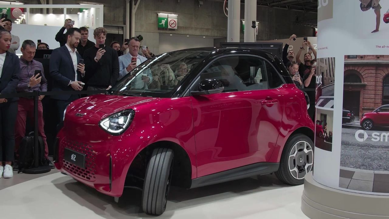 Red Smart #2 with a black roof on the Smart stand at Paris Motor Show 2026, viewed from the front three-quarter as visitors take photos