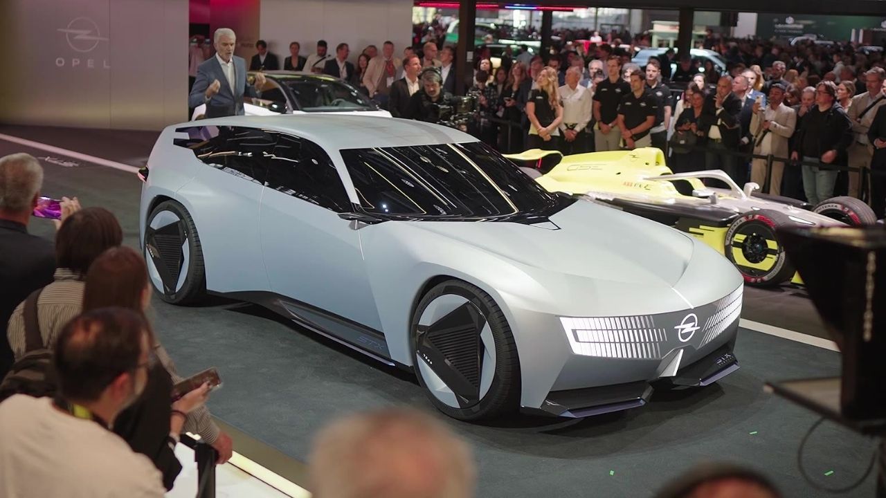 Silver Vauxhall STX Concept, shown with Opel badging on the Opel stand at Paris Motor Show 2026, viewed from the front three-quarter beside a Formula E car