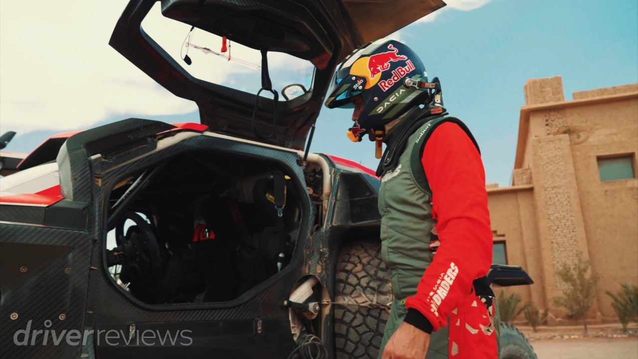 Dacia Sandrider rally raid car with a helmeted team member beside the open cockpit